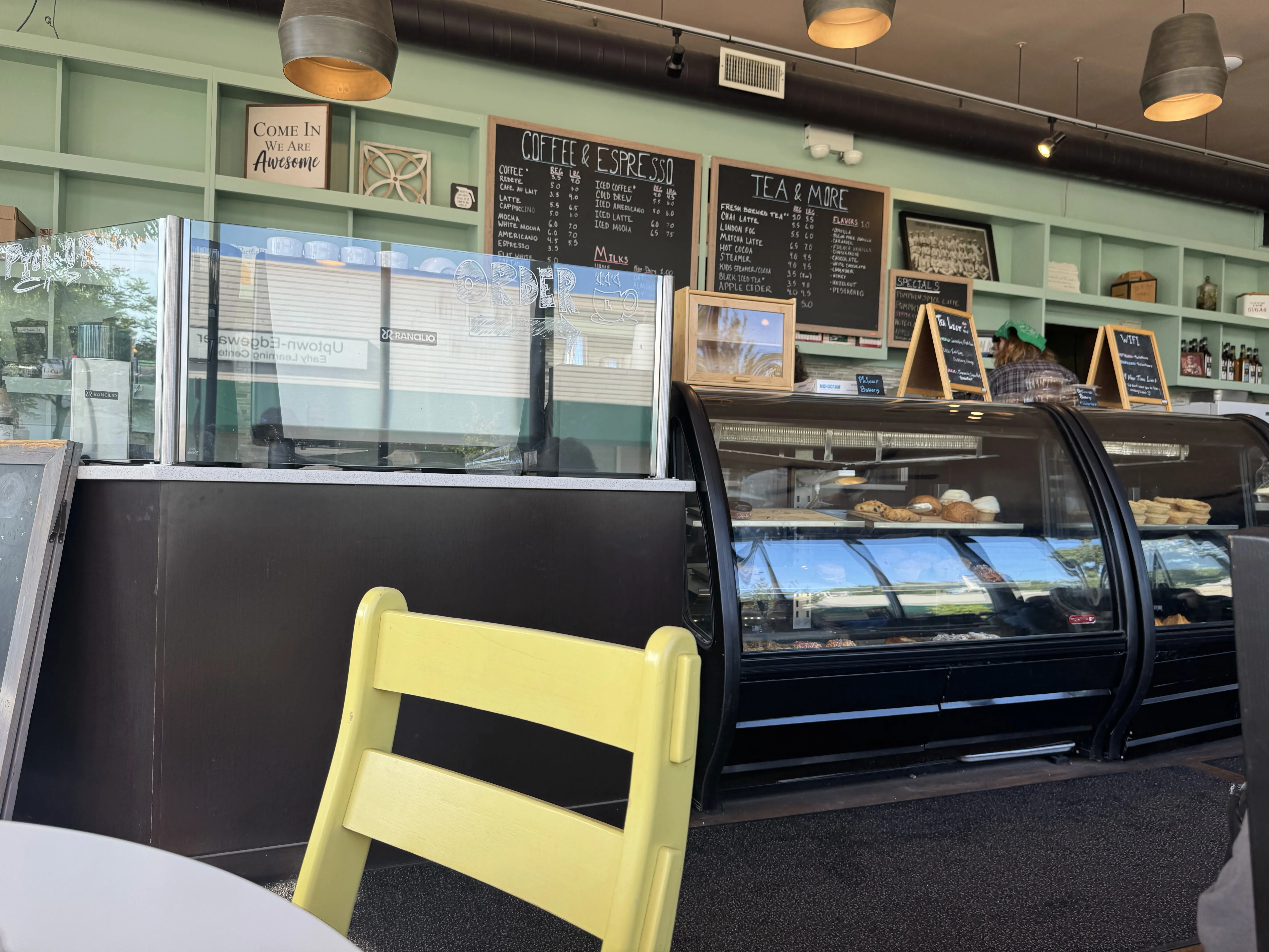 Do y'all appreciate my high-effort 'minimize people + their faces in the frame' techniques? Front view of the cafe. Pastry shelves are visible with chalk boards and shelves in the back.