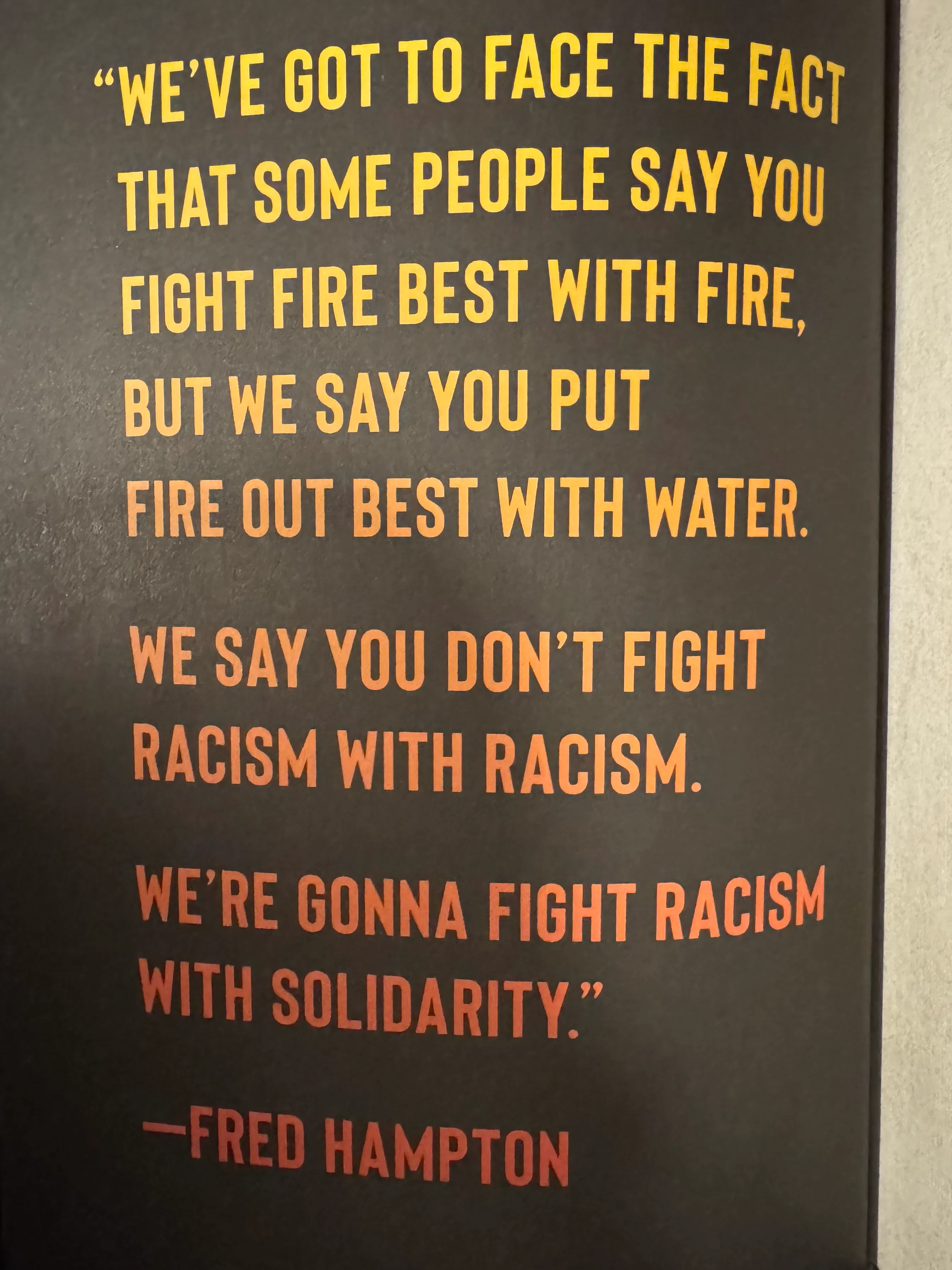 Yellow-to-red gradient text reading: "We've got to face the fact that some people say you fight fire best with fire, but we say you put fire out best with water. We don't fight racism with racism. We're gonna fight racism with solidarity."" -Fred Hampton
