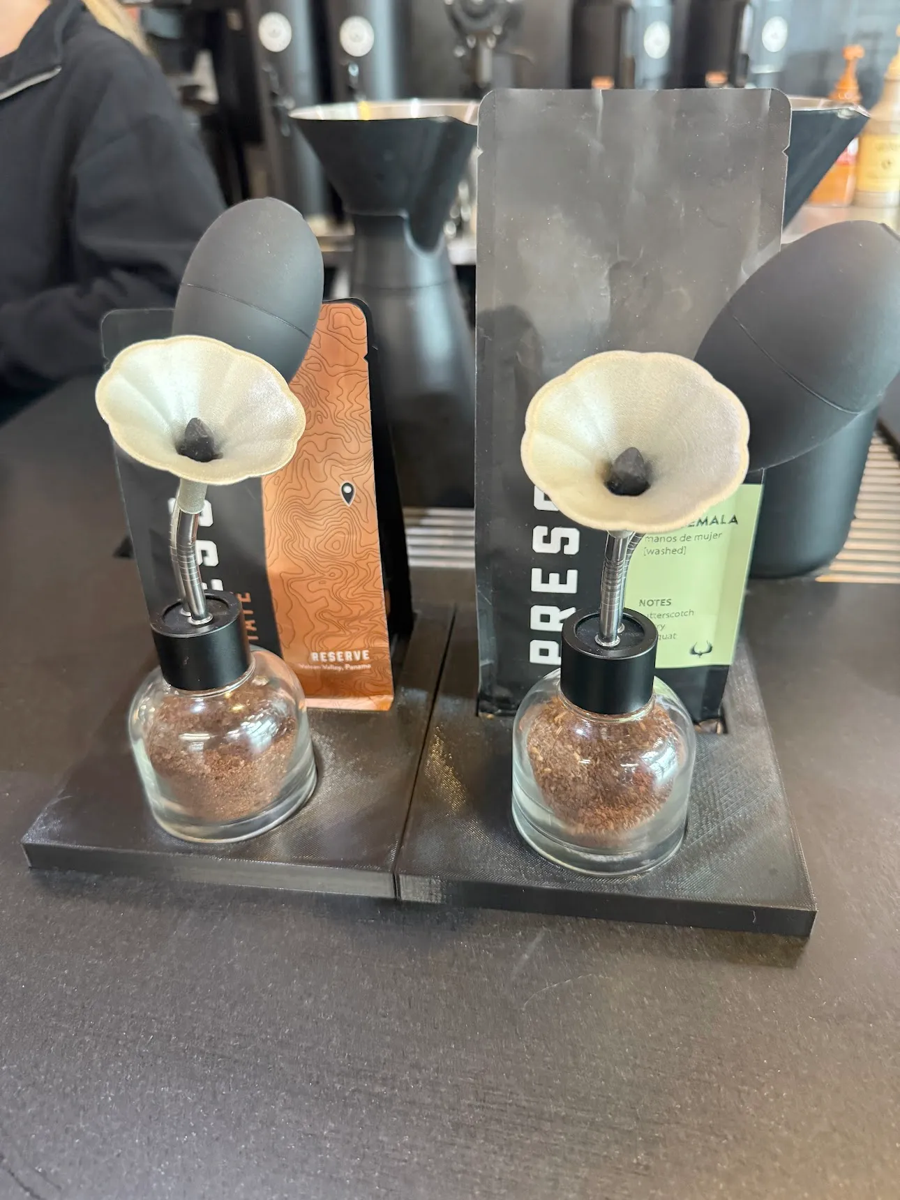 Two glass perfume-aroma bottle things with ground coffee in their glass bodies. There is a squeeze bulb and a little horn.