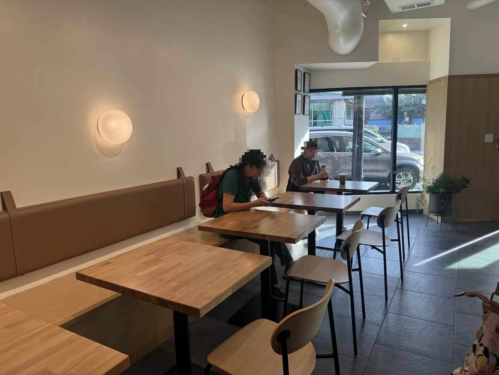 Back-facing-front photo of the cafe seating area. 5 tables visible, with booth seating on the left, and chairs on the right.