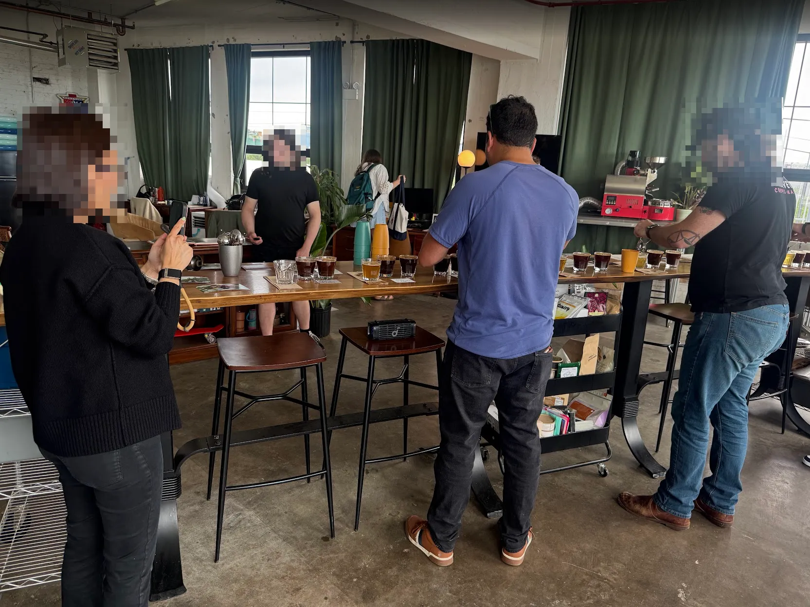 A bunch of folks (with blurred faces) gathered around the long table, doing various tastings